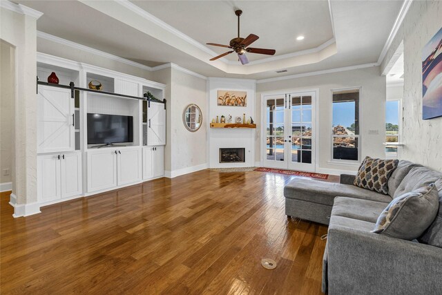 living room featuring ceiling fan, a raised ceiling, hardwood / wood-style floors, a barn door, and crown molding