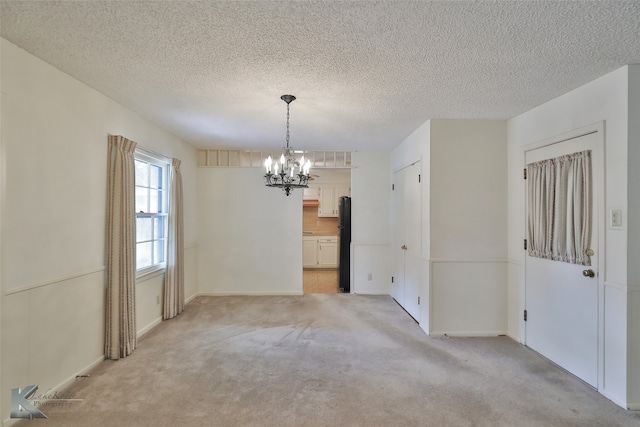 empty room featuring light carpet, a textured ceiling, and an inviting chandelier