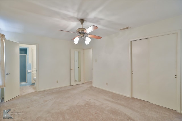 unfurnished bedroom with ceiling fan, a closet, light colored carpet, and ensuite bathroom