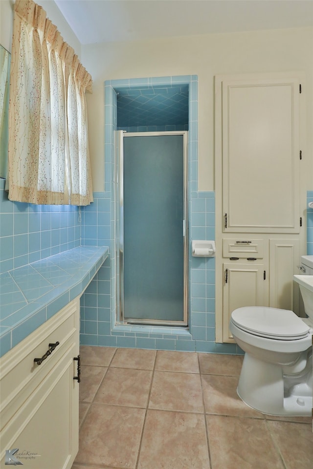 bathroom featuring a shower with door, toilet, tile patterned floors, tile walls, and vanity