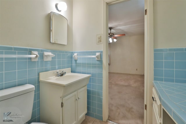 bathroom with tile walls, toilet, vanity, and ceiling fan