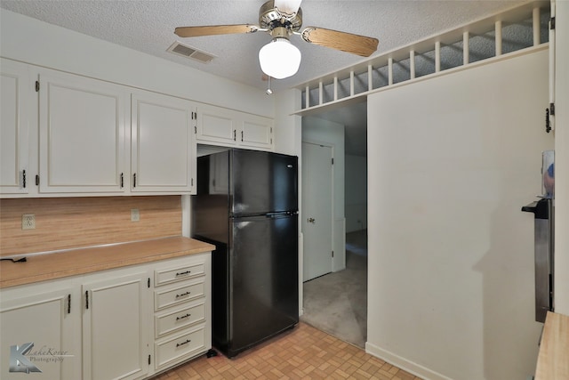 kitchen featuring a textured ceiling, light carpet, ceiling fan, white cabinetry, and black refrigerator