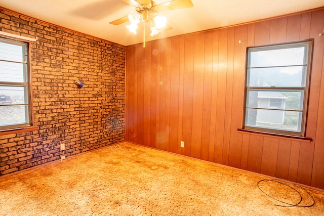 spare room featuring ceiling fan, wood walls, carpet flooring, and brick wall