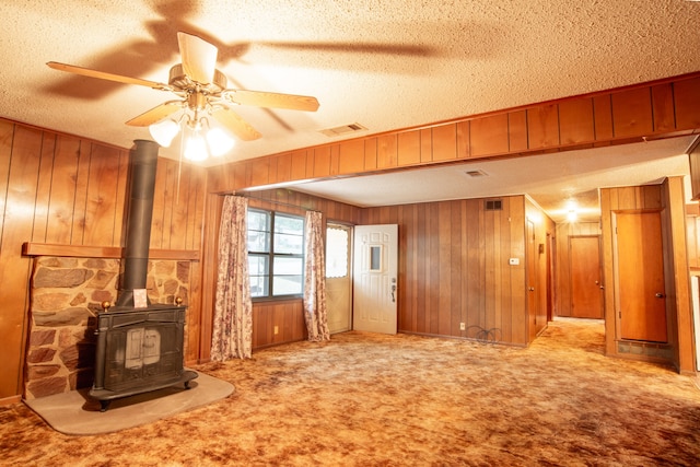 unfurnished living room featuring a wood stove, a textured ceiling, light carpet, and wood walls