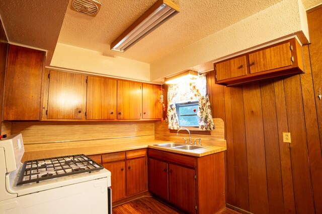 kitchen featuring dark hardwood / wood-style floors, a textured ceiling, wooden walls, sink, and stove