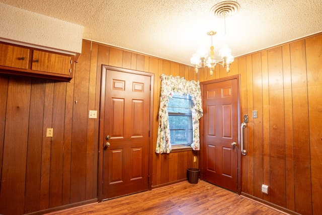 foyer entrance with wood walls, a textured ceiling, hardwood / wood-style flooring, and a chandelier