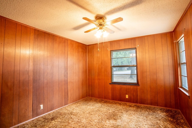 empty room featuring a textured ceiling, wooden walls, ceiling fan, and carpet floors