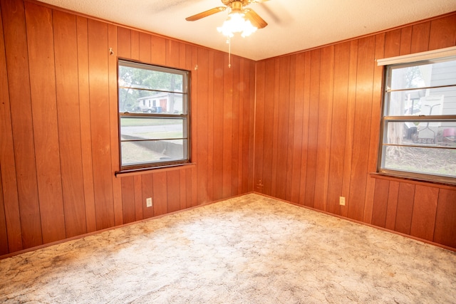 empty room featuring ceiling fan, wooden walls, light colored carpet, and a textured ceiling