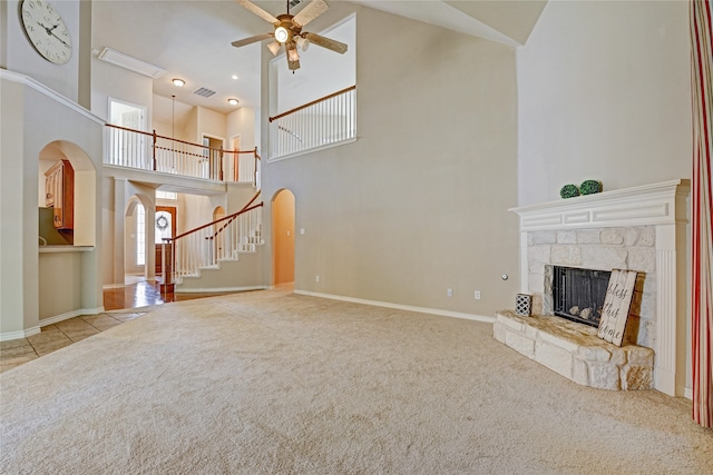 unfurnished living room featuring a stone fireplace, ceiling fan, light colored carpet, and a high ceiling