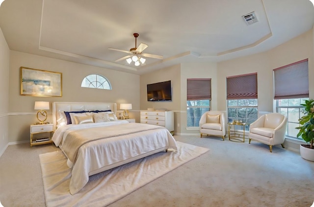 carpeted bedroom with a ceiling fan, a tray ceiling, baseboards, and visible vents