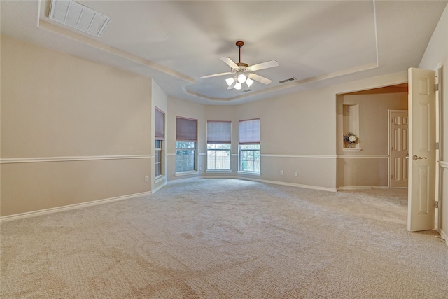 spare room with a tray ceiling, visible vents, and baseboards