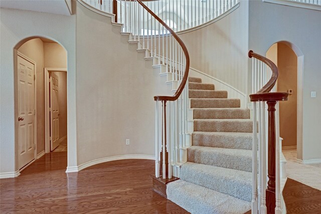 stairs with ceiling fan, hardwood / wood-style floors, and a towering ceiling