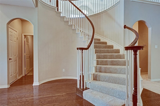 stairs featuring arched walkways, a high ceiling, baseboards, and wood finished floors