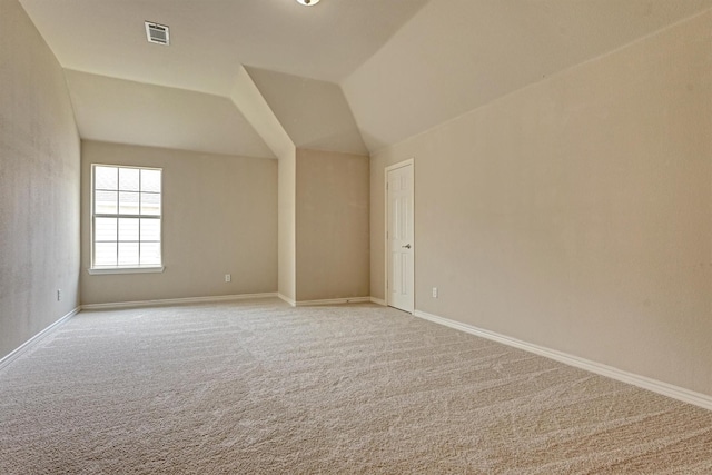 additional living space featuring light carpet, visible vents, baseboards, and lofted ceiling