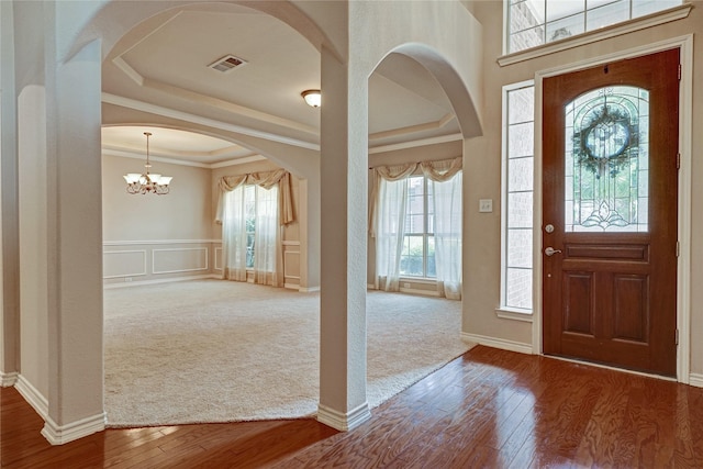 entrance foyer featuring visible vents, crown molding, hardwood / wood-style flooring, a decorative wall, and a raised ceiling