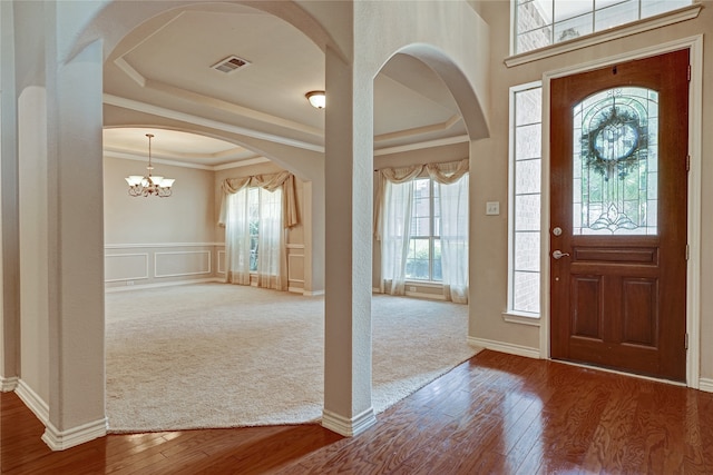 carpeted foyer entrance featuring a tray ceiling, crown molding, and a notable chandelier