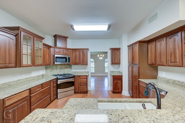 kitchen featuring appliances with stainless steel finishes, light wood-type flooring, sink, and light stone countertops