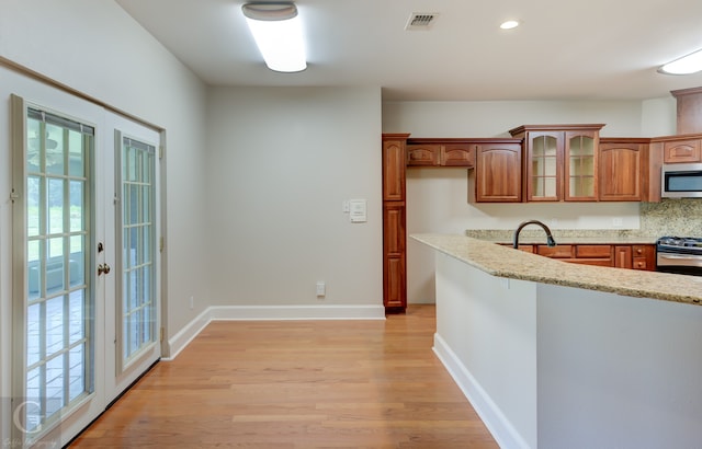 kitchen with light stone countertops, stainless steel appliances, light hardwood / wood-style flooring, and decorative backsplash