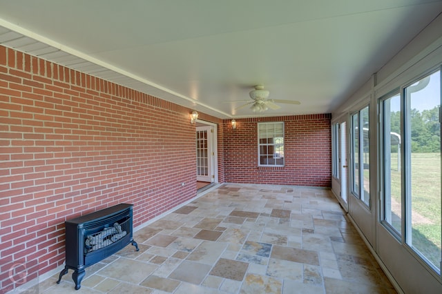 unfurnished sunroom featuring ceiling fan and a wood stove