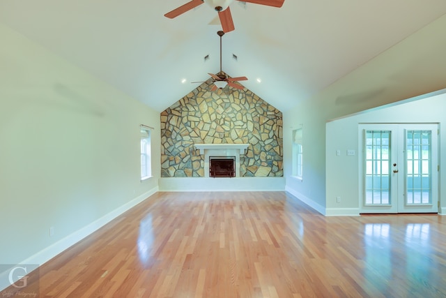 unfurnished living room featuring light hardwood / wood-style flooring, lofted ceiling, ceiling fan, a stone fireplace, and french doors