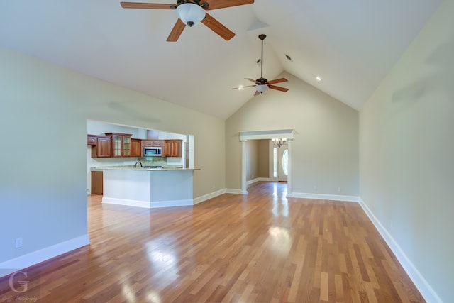 unfurnished living room featuring light hardwood / wood-style flooring, high vaulted ceiling, sink, and ceiling fan with notable chandelier