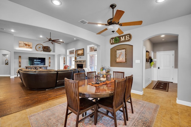 dining space featuring a stone fireplace, light tile patterned floors, and ceiling fan