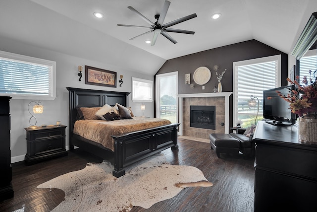 bedroom featuring ceiling fan, dark hardwood / wood-style flooring, lofted ceiling, and a tile fireplace