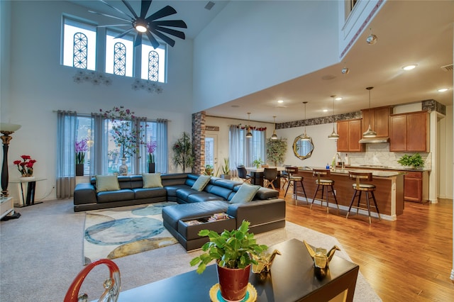 living room featuring a towering ceiling, sink, and light colored carpet