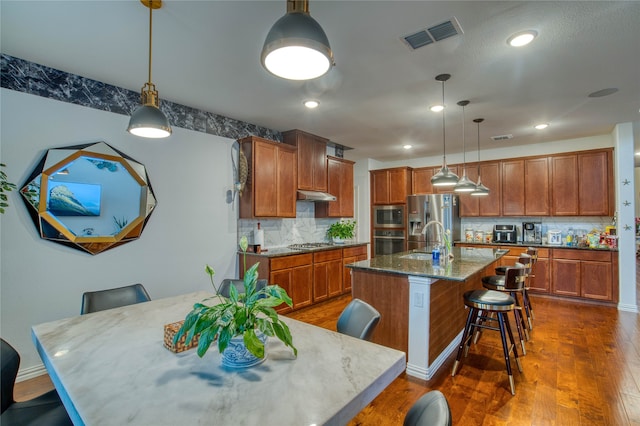 kitchen featuring stainless steel appliances, dark hardwood / wood-style floors, a center island with sink, backsplash, and sink