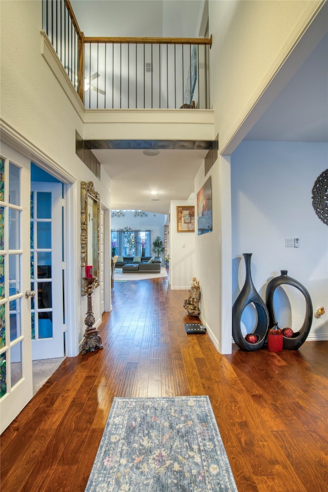 hallway with french doors, a towering ceiling, and wood-type flooring