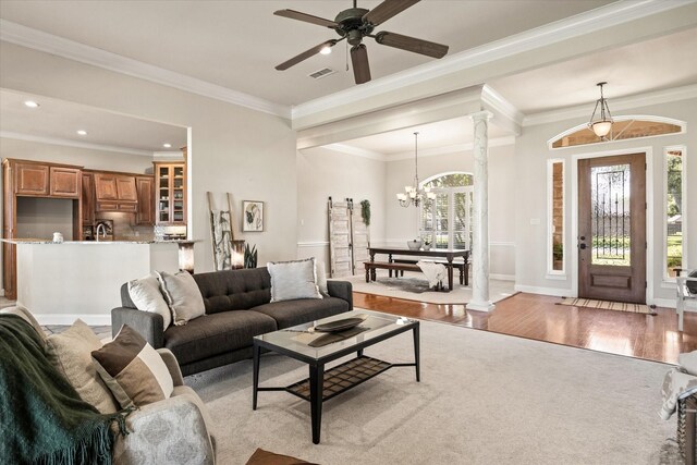 living room featuring decorative columns, crown molding, ceiling fan with notable chandelier, and light hardwood / wood-style floors