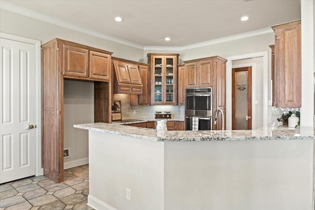 kitchen with double oven, tasteful backsplash, light stone counters, kitchen peninsula, and crown molding