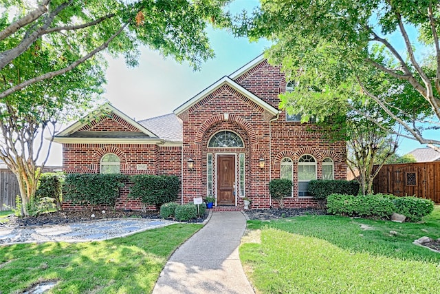 traditional-style house featuring a shingled roof, brick siding, fence, and a front lawn