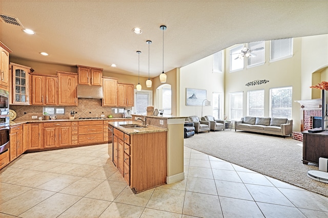 kitchen featuring backsplash, light carpet, a brick fireplace, light stone countertops, and sink