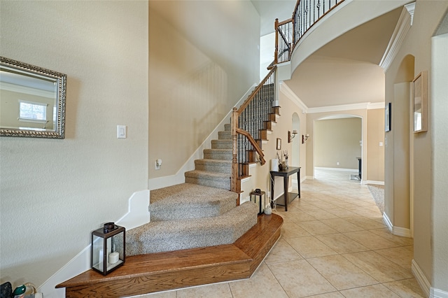 stairs with tile patterned flooring, ornamental molding, and a towering ceiling