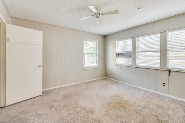 unfurnished room featuring ceiling fan, light colored carpet, wooden walls, and a textured ceiling