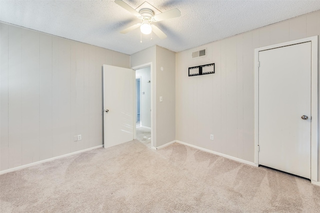 unfurnished bedroom featuring wooden walls, light colored carpet, a textured ceiling, and ceiling fan