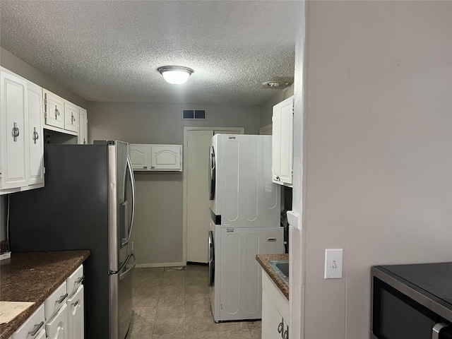 kitchen featuring stacked washer and clothes dryer, stainless steel appliances, a textured ceiling, and white cabinets