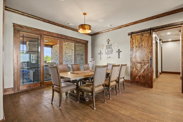 dining room featuring visible vents, baseboards, a barn door, ornamental molding, and wood finished floors