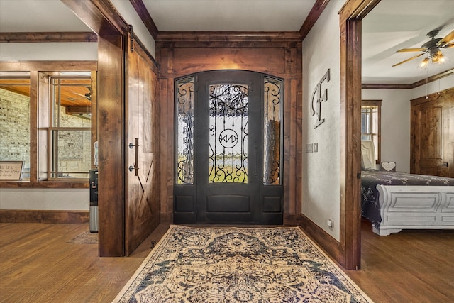 foyer featuring crown molding, hardwood / wood-style floors, ceiling fan, and a barn door