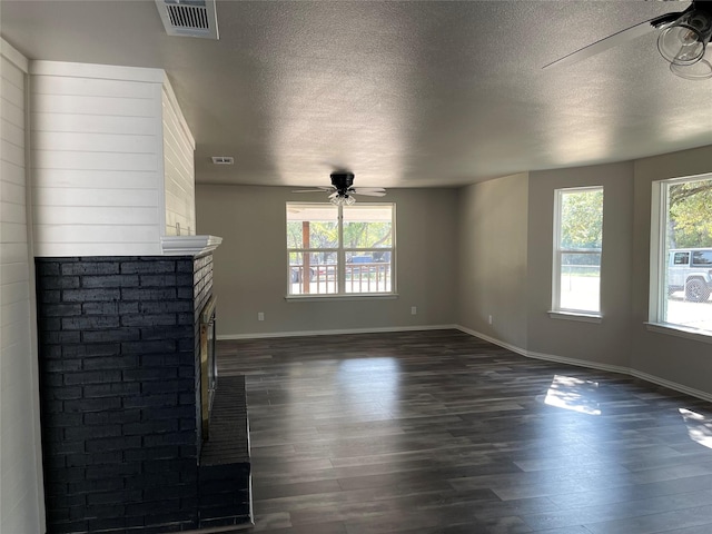 unfurnished living room featuring dark wood-style floors, a brick fireplace, visible vents, and a ceiling fan