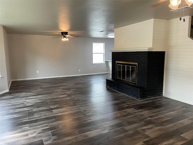 unfurnished living room with a ceiling fan, dark wood-type flooring, a brick fireplace, a textured ceiling, and baseboards