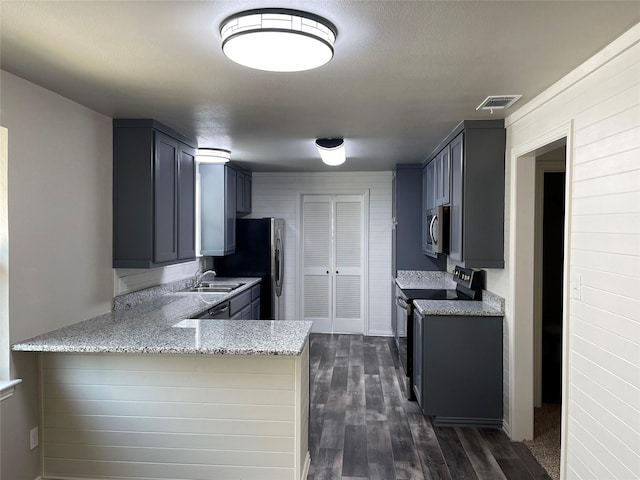 kitchen featuring light stone counters, a peninsula, a sink, visible vents, and appliances with stainless steel finishes