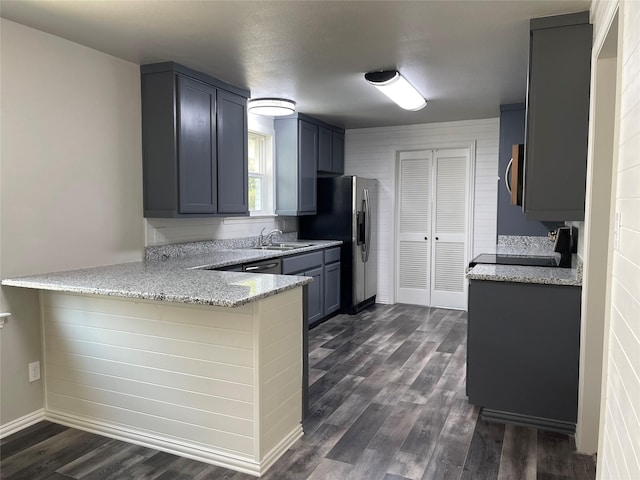 kitchen featuring appliances with stainless steel finishes, light stone counters, dark wood-type flooring, a peninsula, and a sink