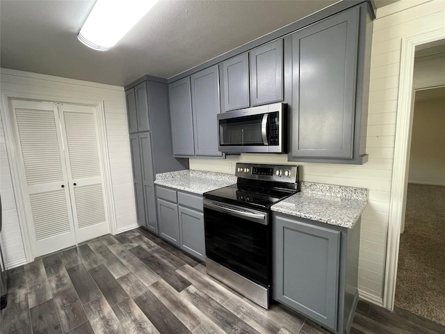 kitchen with stainless steel appliances, gray cabinets, light stone counters, and dark wood-style flooring