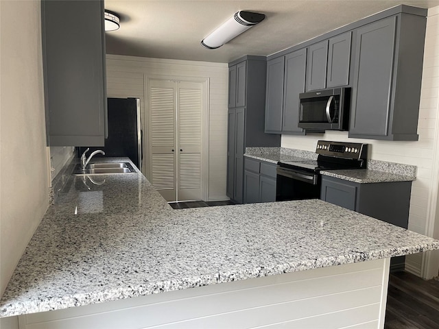 kitchen featuring gray cabinets, stainless steel microwave, black electric range oven, a sink, and a peninsula