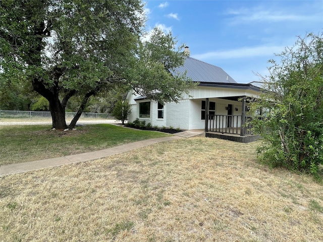 view of front of property featuring metal roof, a porch, fence, a front lawn, and a chimney