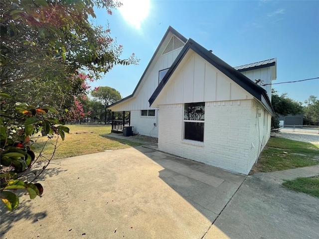 rear view of property featuring brick siding, a yard, board and batten siding, a patio area, and central AC