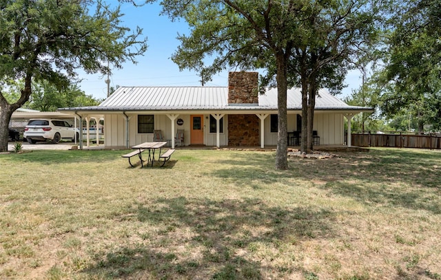 rear view of house with metal roof, fence, a lawn, board and batten siding, and a chimney