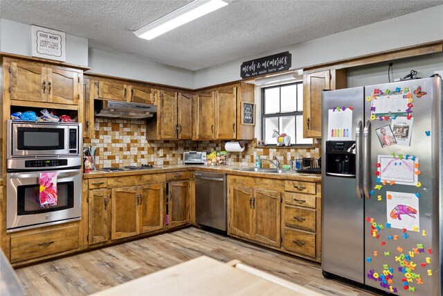 kitchen featuring decorative backsplash, stainless steel appliances, sink, and light hardwood / wood-style floors